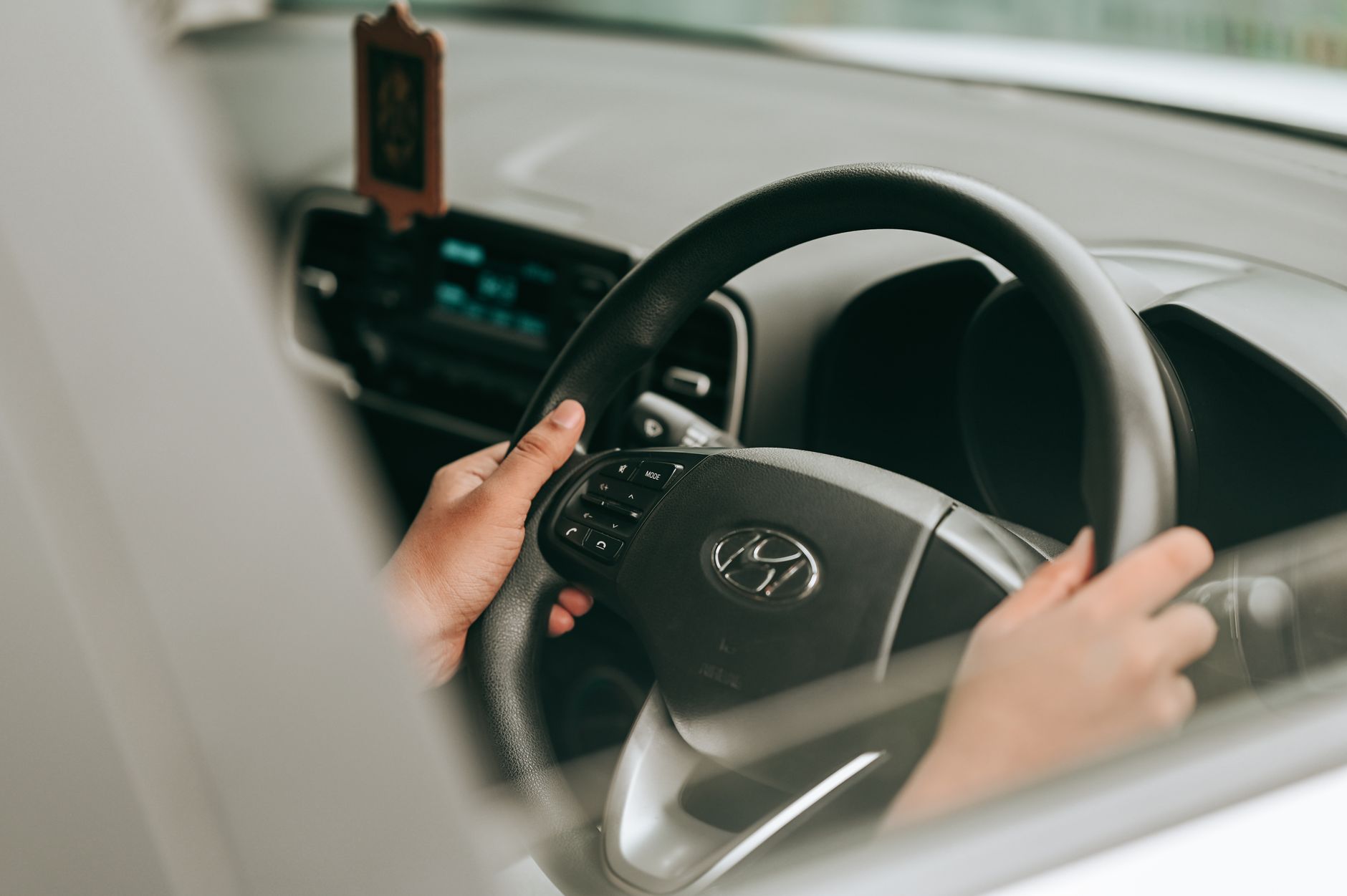 A driver's view from inside the car with hands on the wheel and mirror in view